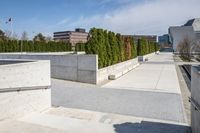 the empty concrete walkway leads into a building complex with trees and greenery growing along the wall