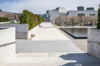 the empty concrete walkway leads into a building complex with trees and greenery growing along the wall