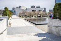 the empty concrete walkway leads into a building complex with trees and greenery growing along the wall