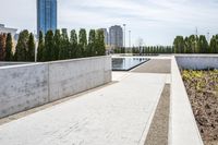 the empty concrete walkway leads into a building complex with trees and greenery growing along the wall