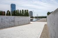 the empty concrete walkway leads into a building complex with trees and greenery growing along the wall