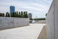 the empty concrete walkway leads into a building complex with trees and greenery growing along the wall