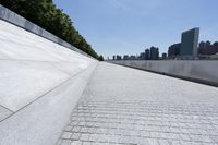 an empty walkway at the waterfront next to water and skyscrapers in the background of a sunny day