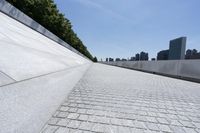 an empty walkway at the waterfront next to water and skyscrapers in the background of a sunny day