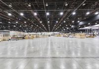 an empty warehouse with lots of cardboard boxes and chairs in it, lights on overhead, and floor of warehouse
