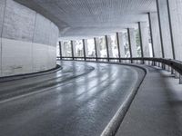 a street is empty as the ground in an urban setting is wet and concrete with a long curved gray line in front of it