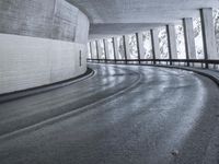 a street is empty as the ground in an urban setting is wet and concrete with a long curved gray line in front of it