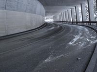 a street is empty as the ground in an urban setting is wet and concrete with a long curved gray line in front of it