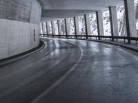 a street is empty as the ground in an urban setting is wet and concrete with a long curved gray line in front of it