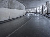 a street is empty as the ground in an urban setting is wet and concrete with a long curved gray line in front of it