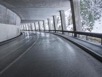 a street is empty as the ground in an urban setting is wet and concrete with a long curved gray line in front of it