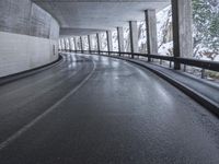 a street is empty as the ground in an urban setting is wet and concrete with a long curved gray line in front of it