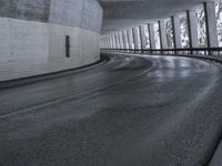 a street is empty as the ground in an urban setting is wet and concrete with a long curved gray line in front of it