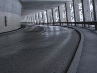 a street is empty as the ground in an urban setting is wet and concrete with a long curved gray line in front of it