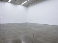 a large empty white room with concrete floors and exposed lighting fixture above the space in the center