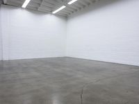 a large empty white room with concrete floors and exposed lighting fixture above the space in the center