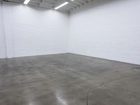 a large empty white room with concrete floors and exposed lighting fixture above the space in the center