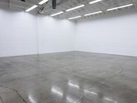 a large empty white room with concrete floors and exposed lighting fixture above the space in the center