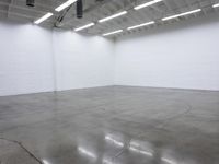 a large empty white room with concrete floors and exposed lighting fixture above the space in the center