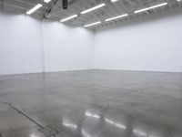 a large empty white room with concrete floors and exposed lighting fixture above the space in the center