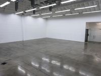 a large empty white room with concrete floors and exposed lighting fixture above the space in the center