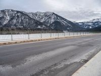 an empty mountain road in winter with snow on the ground and trees near by,