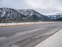 an empty mountain road in winter with snow on the ground and trees near by,