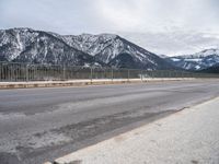 an empty mountain road in winter with snow on the ground and trees near by,