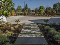 a small concrete walk way leading to an enclosed backyard area with grass, bushes and trees