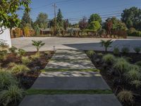 a small concrete walk way leading to an enclosed backyard area with grass, bushes and trees