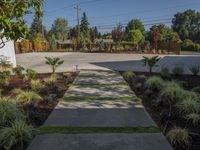 a small concrete walk way leading to an enclosed backyard area with grass, bushes and trees