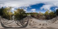 the fisheye lens view of an enclosed bridge in the middle of some trees and grass