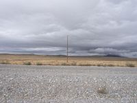 view from a gravel road looking toward an out - range setting with dark clouds overhead