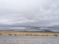 view from a gravel road looking toward an out - range setting with dark clouds overhead