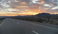 an open highway with mountains and hills in the distance at sunset in the desert setting