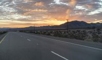 an open highway with mountains and hills in the distance at sunset in the desert setting