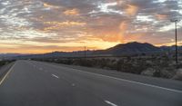 an open highway with mountains and hills in the distance at sunset in the desert setting