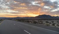 an open highway with mountains and hills in the distance at sunset in the desert setting