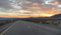 an open highway with mountains and hills in the distance at sunset in the desert setting