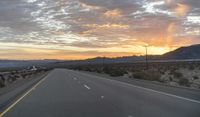 an open highway with mountains and hills in the distance at sunset in the desert setting