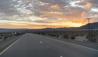 an open highway with mountains and hills in the distance at sunset in the desert setting