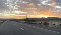 an open highway with mountains and hills in the distance at sunset in the desert setting