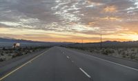 an open highway with mountains and hills in the distance at sunset in the desert setting