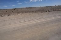 an empty dirt road in the middle of a desert area with a white and black fire hydrant near it