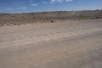 an empty dirt road in the middle of a desert area with a white and black fire hydrant near it