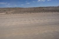 an empty dirt road in the middle of a desert area with a white and black fire hydrant near it