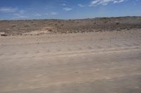 an empty dirt road in the middle of a desert area with a white and black fire hydrant near it