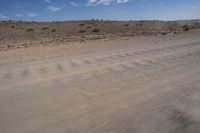 an empty dirt road in the middle of a desert area with a white and black fire hydrant near it