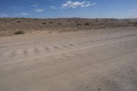 an empty dirt road in the middle of a desert area with a white and black fire hydrant near it