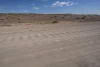 an empty dirt road in the middle of a desert area with a white and black fire hydrant near it